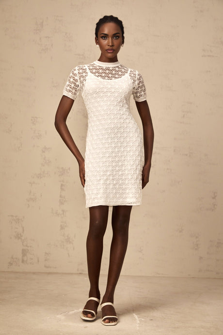 A white semisheer knit mini dress on a model against a plain background showcasing the dresses short length and delicate fabric texture