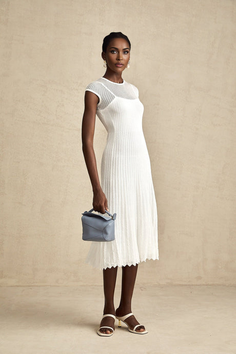 A white semisheer midi dress with scalloped hem details and a flowing silhouette worn by a model against a plain background