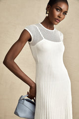 A white semisheer midi dress with scalloped hem details named Liane worn by a model standing against a plain background