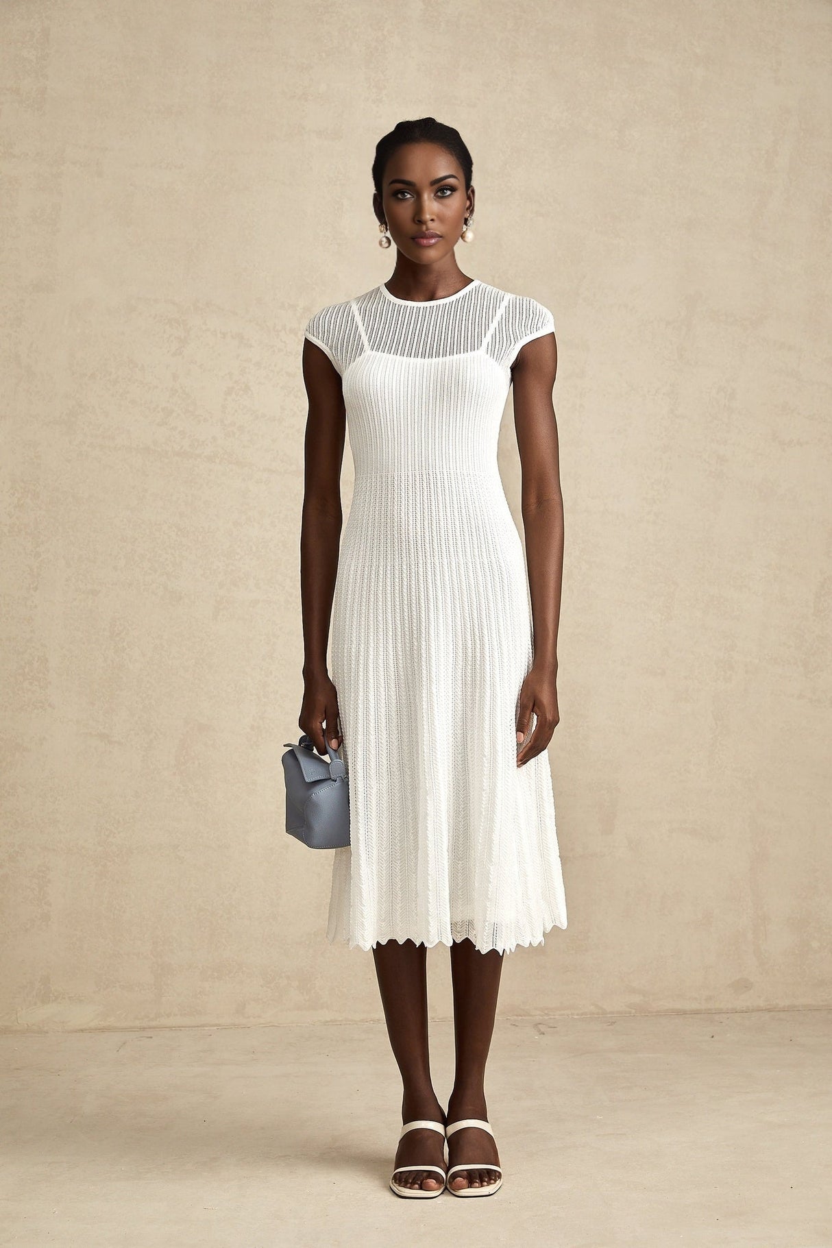 A white semisheer midi dress with scalloped hem details worn by a model standing against a plain background