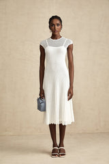 A white semisheer midi dress with scalloped hem details worn by a model standing against a plain background