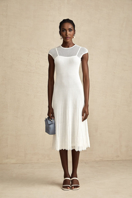 A white semisheer midi dress with scalloped hem details worn by a model standing against a plain background