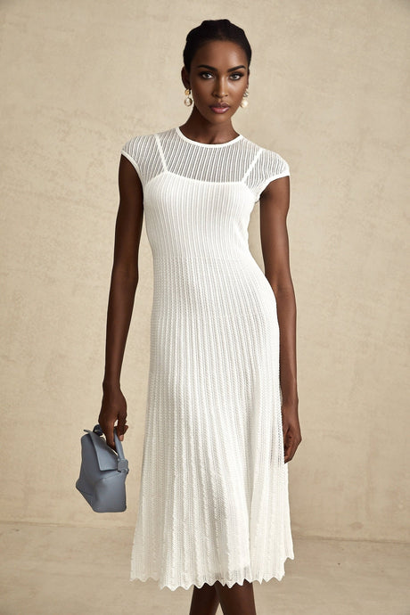 A white semisheer midi dress with scalloped hem named Liane worn by a model standing against a plain background