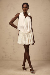 A white sleeveless halterneck top with floral applique detailing worn by a model against a plain background