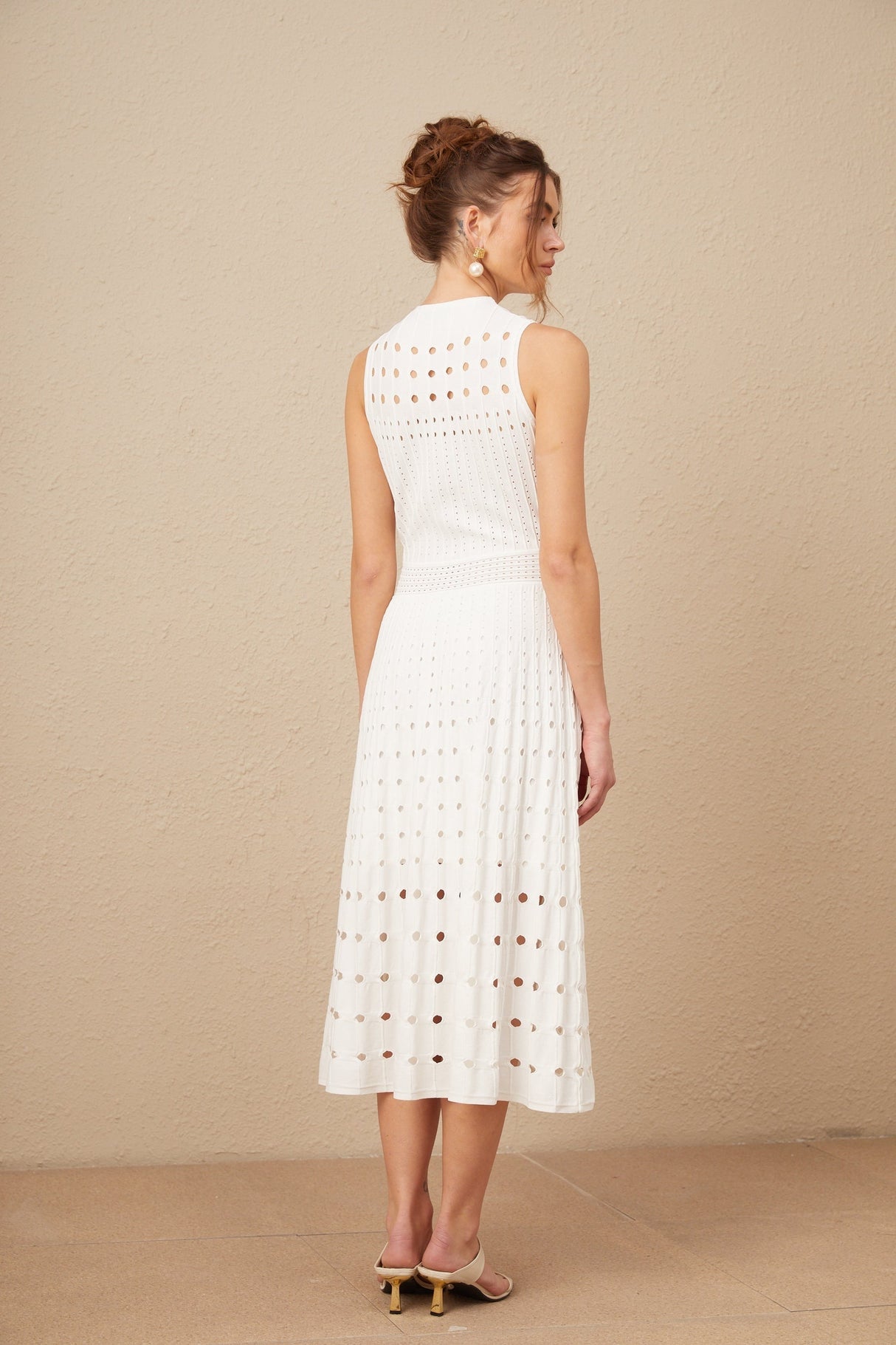 A white sleeveless knitted midi dress with cut out details modeled on a woman against a plain background