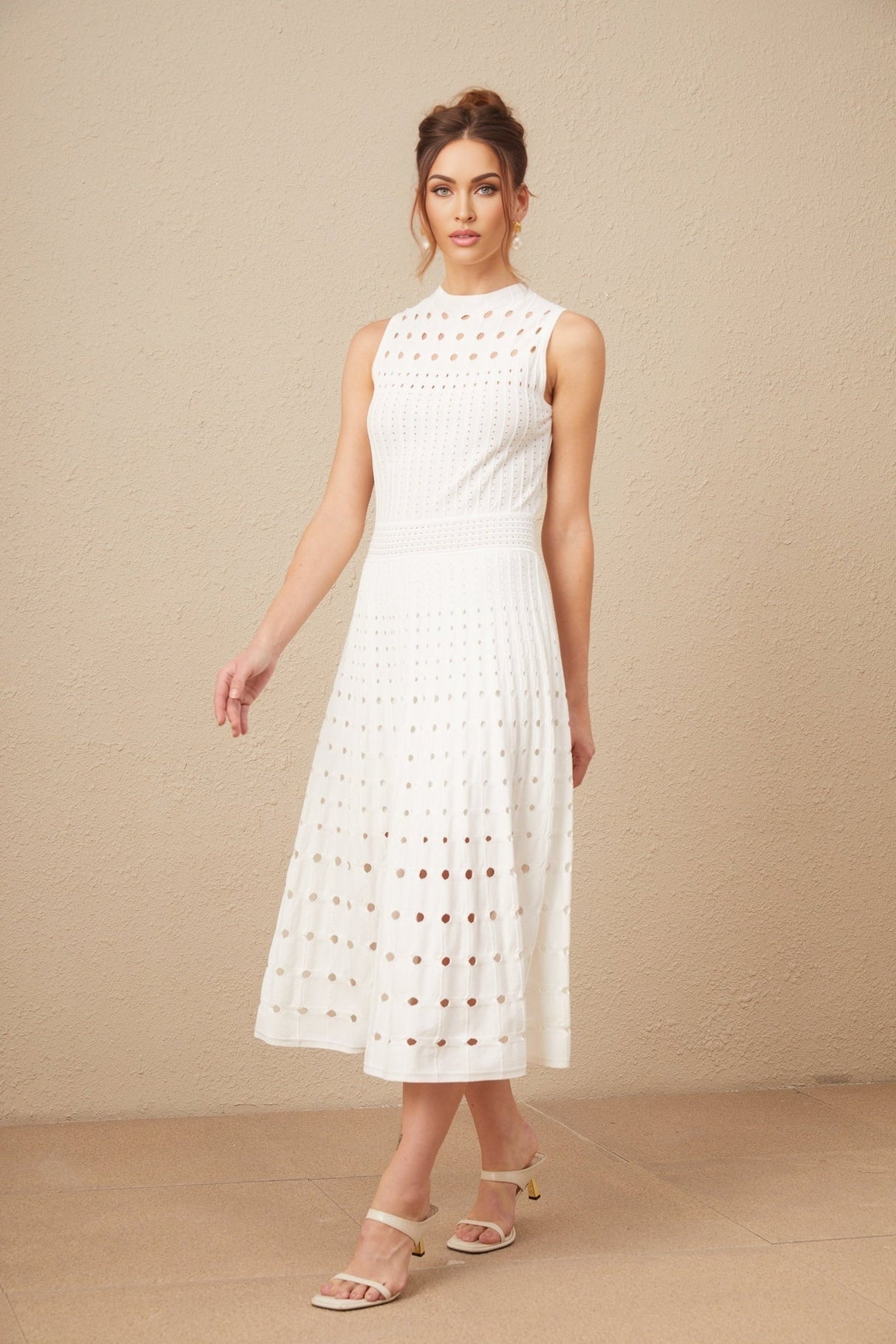 A white sleeveless knitted midi dress with cutout details worn by a model standing against a plain background