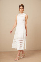 A white sleeveless knitted midi dress with cutout details worn by a model standing against a plain background