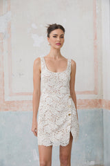 A white sleeveless mini dress made of corded lace featuring a delicate floral pattern and a short hemline