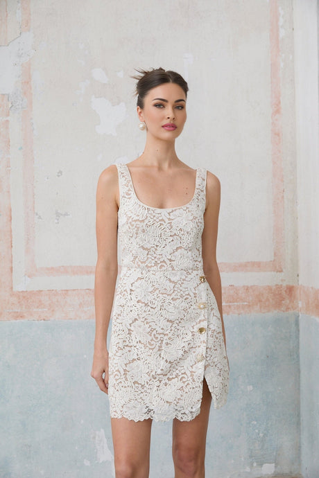 A white sleeveless mini dress made of corded lace featuring a delicate floral pattern and a short hemline