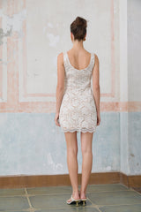 A white sleeveless mini dress made of corded lace featuring a fitted silhouette and delicate floral patterns throughout the fabric