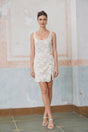 A white sleeveless mini dress made of corded lace featuring a short hemline and intricate floral patterns throughout the fabric