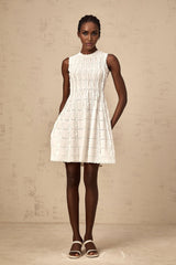 A white sleeveless mini dress with a knit fabric and ruffled details worn by a model standing against a plain background