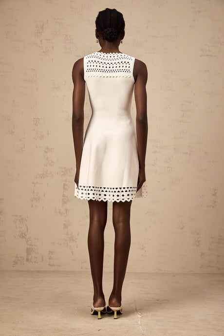 A white sleeveless mini dress with cutout details and a knitted texture worn by a model standing against a plain background