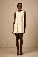 A white sleeveless mini dress with wavy details named Axelle worn by a model standing against a plain background