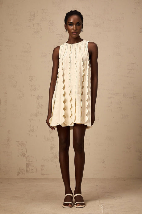 A white sleeveless mini dress with wavy details named Axelle worn by a model standing against a plain background