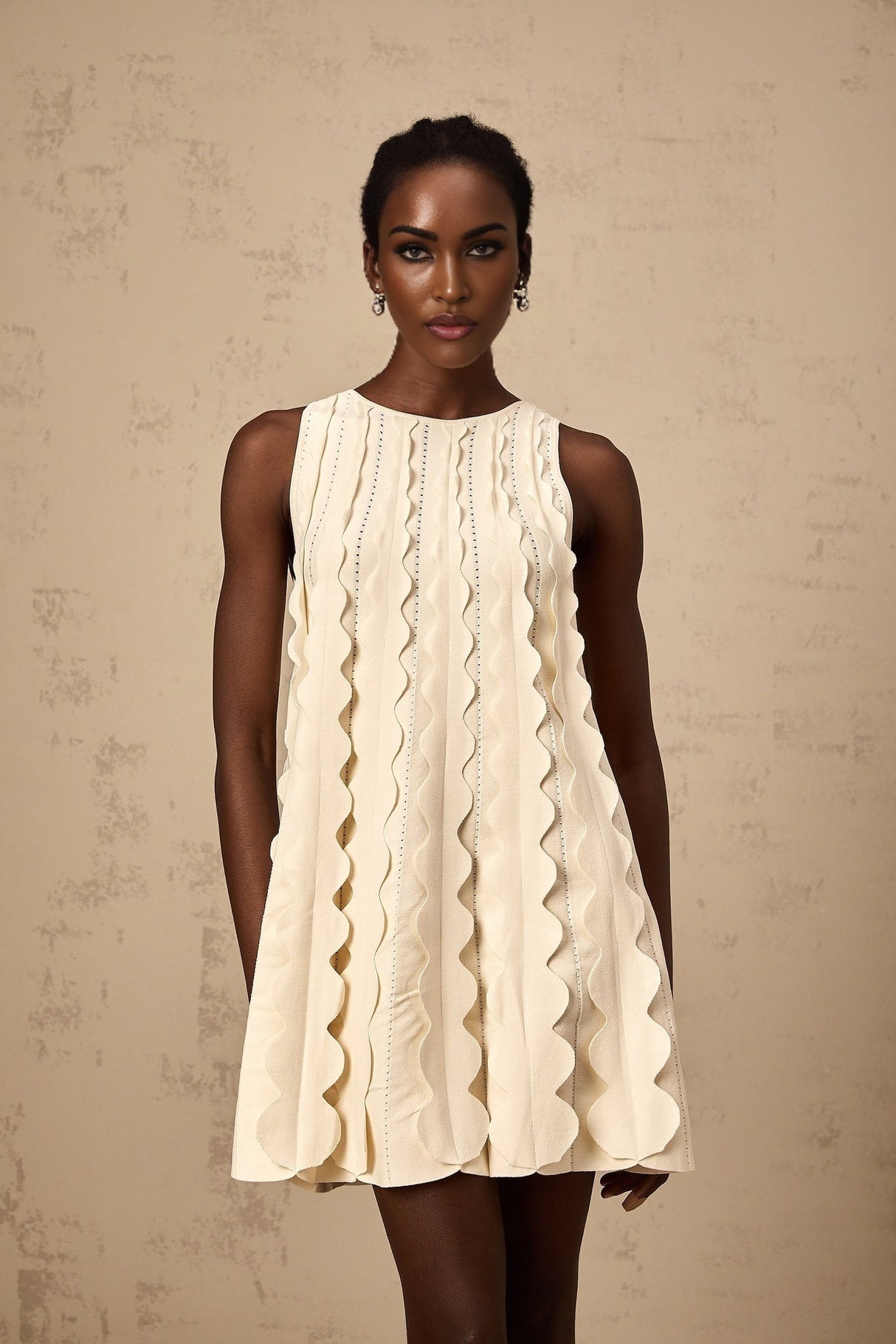 A white sleeveless mini dress with wavy details on a female model named Axelle
