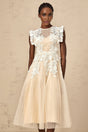 A white tulle midi dress with floral appliques scattered across the bodice and skirt featuring a fitted waist and delicate straps