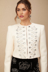 A white tweed jacket adorned with crystal embellishments featuring a classic cut and textured fabric