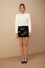 A white tweed jacket adorned with crystal embellishments featuring a classic design and texture