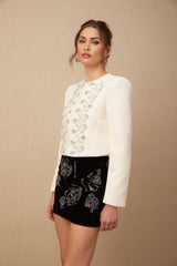 A white tweed jacket adorned with crystal embellishments featuring a classic design and textured fabric