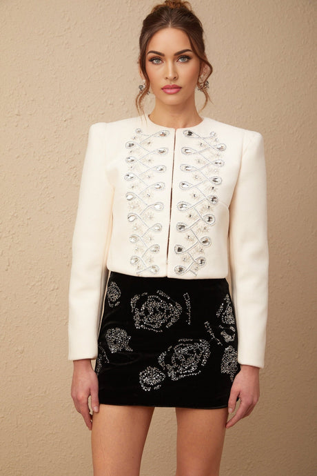 A white tweed jacket adorned with crystal embellishments featuring a classic tailored silhouette and sparkling accents throughout