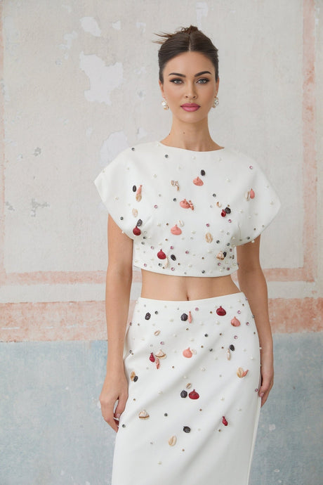 A white twopiece outfit consisting of a sleeveless top and skirt decorated with shell embellishments matching set called Delphine