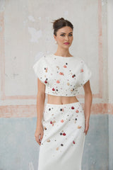 A white twopiece outfit consisting of a top and skirt decorated with shell embellishments named Delphine