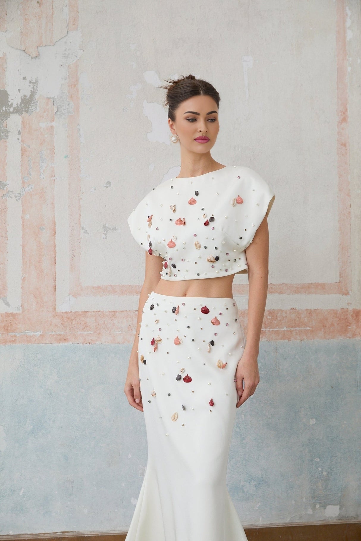A white twopiece outfit featuring a top and skirt adorned with decorative shell embellishments both pieces matching to create a coordinated set