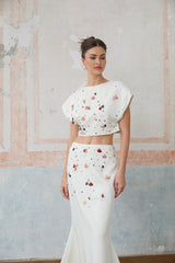A white twopiece outfit featuring a top and skirt adorned with decorative shell embellishments both pieces matching to create a coordinated set