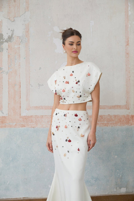 A white twopiece outfit featuring a top and skirt adorned with decorative shell embellishments both pieces matching to create a coordinated set