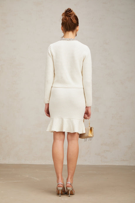 A white waffle knit matching set featuring an embellished cardigan and skirt both with a textured pattern The cardigan has long sleeves and the skirt is knee length The set is adorned with decorative embellishments for a stylish look