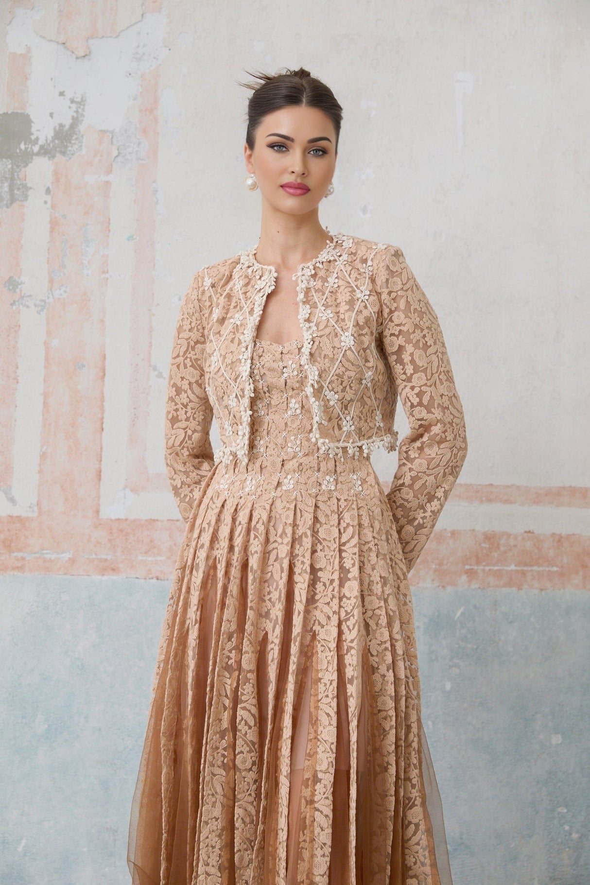 A woman wearing a beige crochet lace cardigan over a matching sleeveless dress standing in a neutral background
