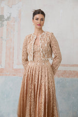 A woman wearing a beige crochet lace cardigan over a matching sleeveless dress standing in a neutral background
