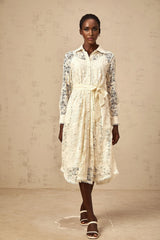A woman wearing a beige midi shirt dress with intricate guipure lace details standing in a neutral setting