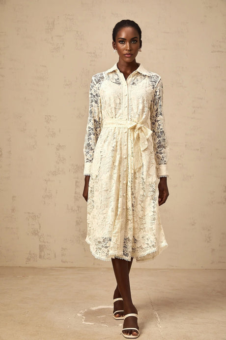 A woman wearing a beige midi shirt dress with intricate guipure lace details standing in a neutral setting
