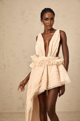 A woman wearing a beige mini dress with an asymmetric hemline and a ribbon design detail across the bodice
