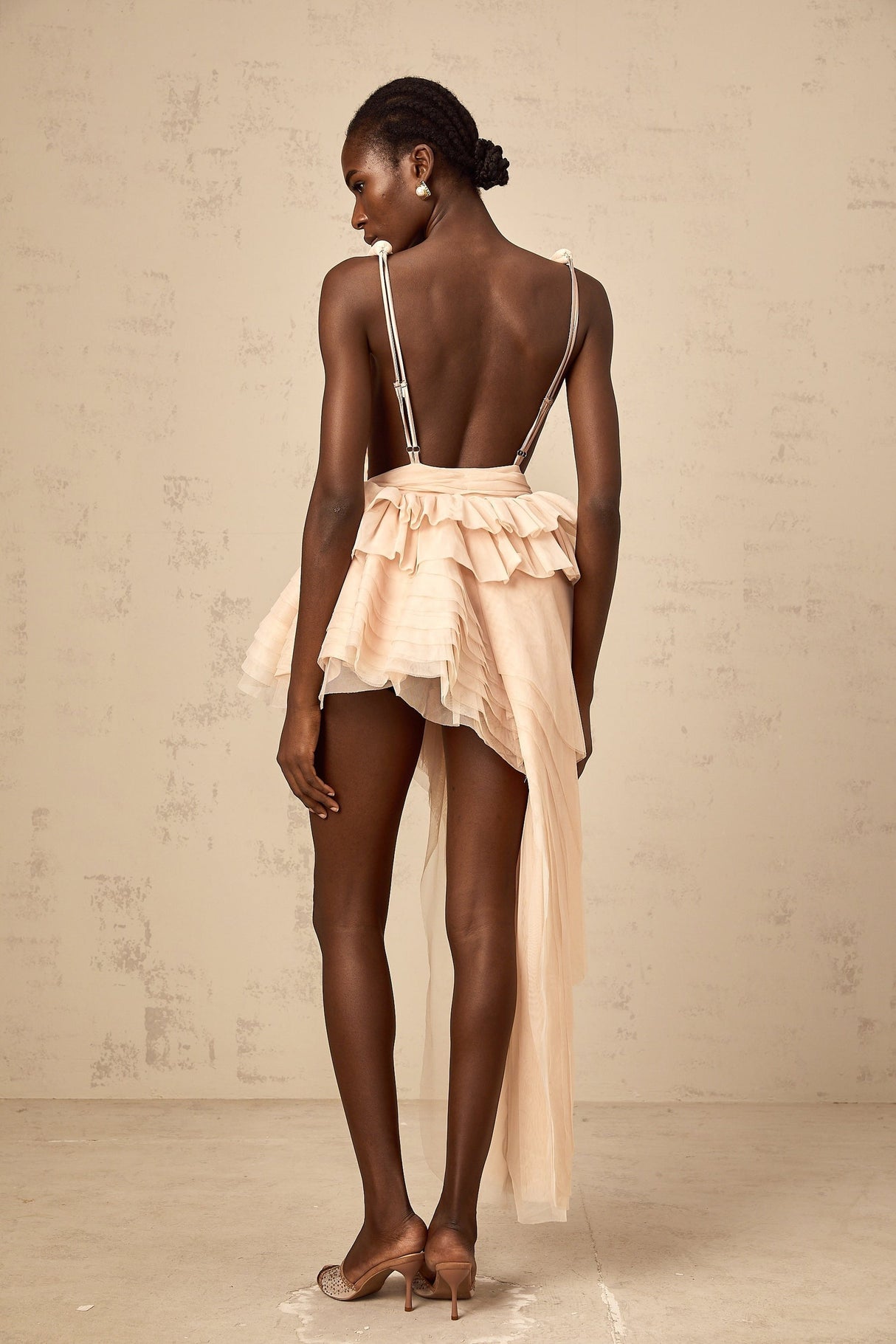 A woman wearing a beige mini dress with asymmetric design featuring ribbon details and a neutral color palette