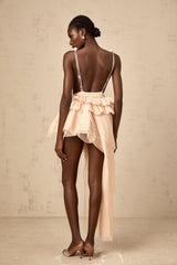 A woman wearing a beige mini dress with asymmetric design featuring ribbon details and a neutral color palette
