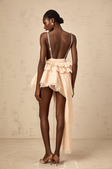 A woman wearing a beige mini dress with asymmetric design featuring ribbon details and a neutral color palette