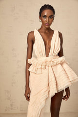 A woman wearing a beige mini dress with asymmetric design featuring ribbon details and neutral tones
