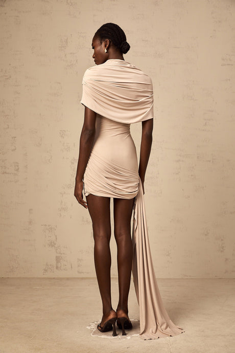 A woman wearing a beige mini dress with capelike sleeves and ruched detailing fitted to the body