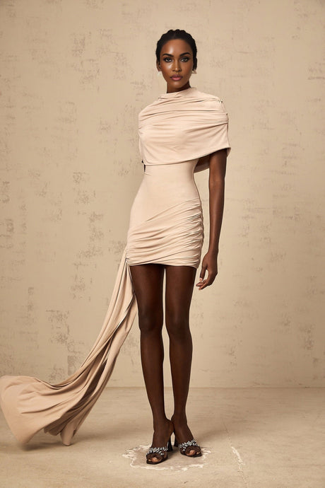 A woman wearing a beige mini dress with capelike sleeves and ruched detailing on the body creating a fitted silhouette