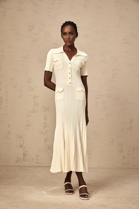 A woman wearing a beige ribbedknit midi dress with a formfitting silhouette and long sleeves standing against a plain background