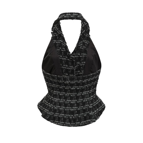 A woman wearing a black and white checked tweed matching set consisting of a sleeveless vest top and a skirt standing against a plain background