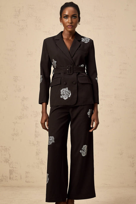 A woman wearing a black blazer and trousers set decorated with studded rose patterns The blazer has a tailored fit and the trousers are slim The outfit is styled as a matching set