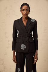 A woman wearing a black blazer and trousers set with roseshaped studs The blazer features a tailored fit and the trousers have a slim cut Both pieces are adorned with metallic studs in floral patterns
