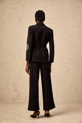 A woman wearing a black blazer and trousers set with studded rose designs The blazer has a tailored fit and the trousers are slim cut Both pieces feature decorative rose patterns made with small studs