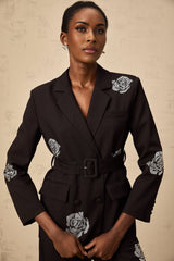 A woman wearing a black blazer and trousers set with studded rose details The blazer features a tailored fit and the trousers are slim cut The outfit is adorned with small metallic studs forming rose patterns