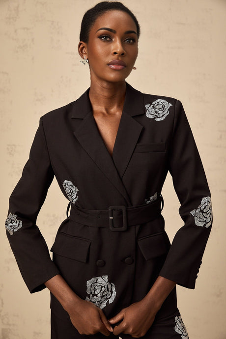 A woman wearing a black blazer and trousers set with studded rose details The blazer features a tailored fit and the trousers are slim cut The outfit is adorned with small metallic studs forming rose patterns