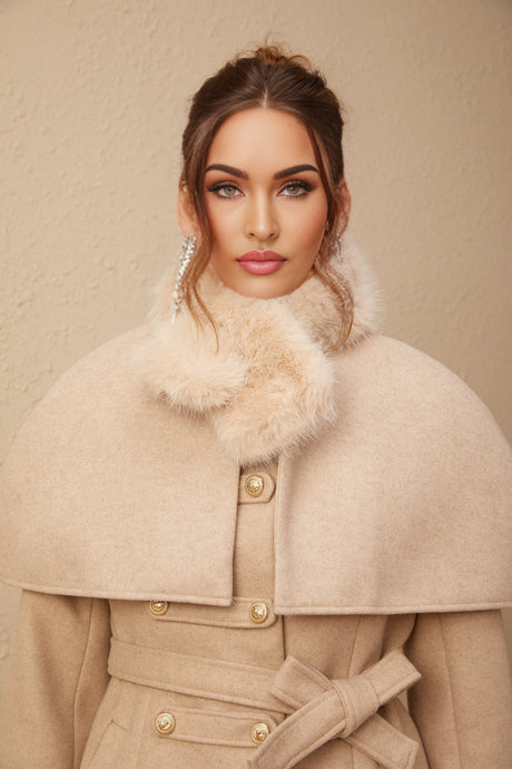 A woman wearing a black faux fur coat with a detachable cape collar standing against a plain background